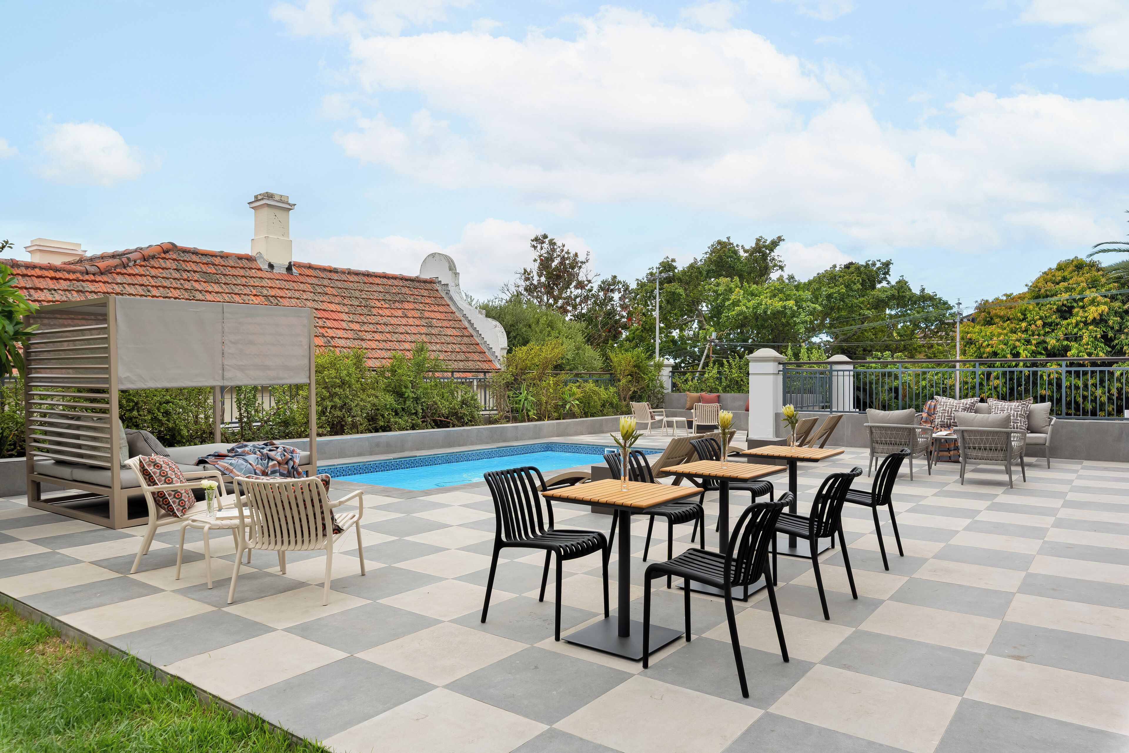 Un patio exterior con piscina, suelo a cuadros y mobiliario de exterior.