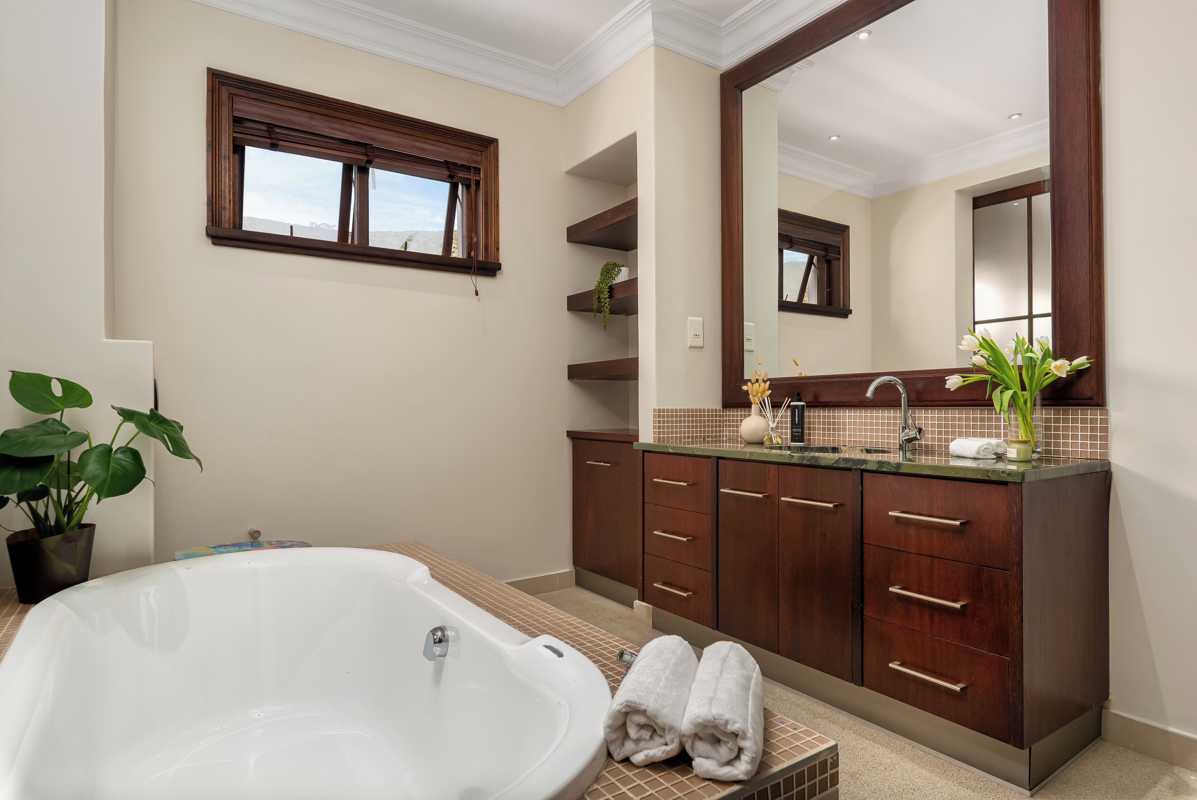 A bathroom with a freestanding bathtub, wooden cabinets, a large mirror, and a potted plant.