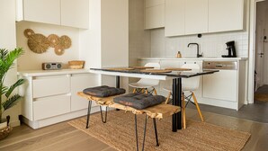Une cuisine moderne avec des meubles blancs, une table en bois avec des coussins et une radio.