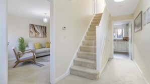 A hallway with a carpeted staircase, a sofa with cushions, a chair, a plant, and a painting on the wall. - Spacious 5-bed Contractor House - Parking Wi-fi (Coventry)