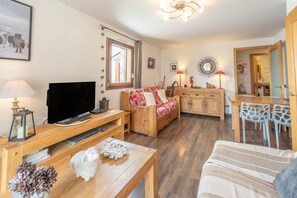 Een woonkamer met een televisie, houten meubels, een bank, een eettafel met stoelen en een keukenhoek.