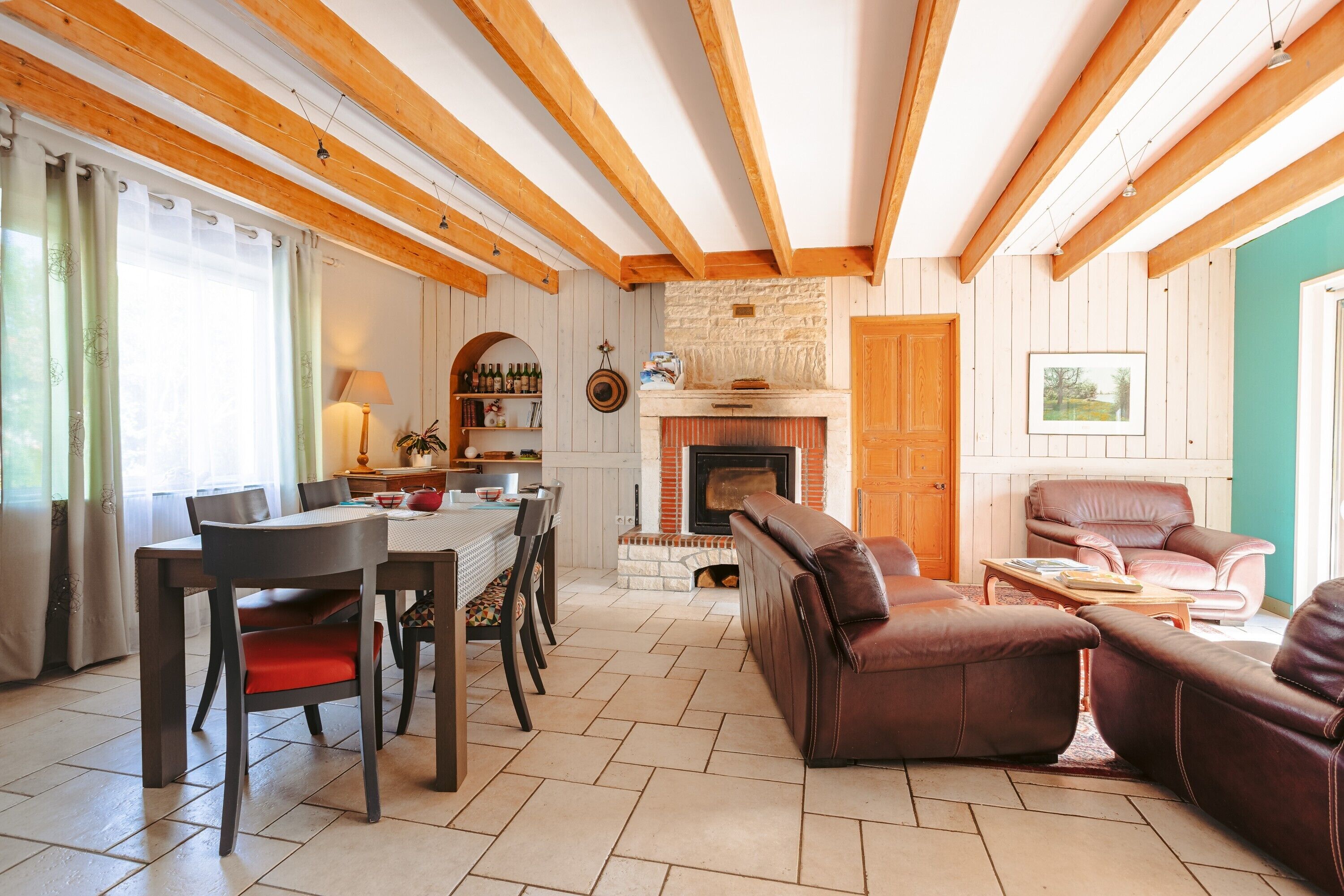 Un salon chaleureux avec une cheminée, des poutres apparentes, un coin repas et des sièges confortables.