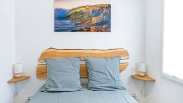 Un dormitorio con cabecera de madera, dos almohadas, lámparas de noche y un cuadro colgado en la pared que muestra una ola.