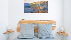 A bed with a wooden headboard, two pillows, bedside lamps, and a wall-mounted picture of a wave. - Silène Guest Room with Wi-Fi and Air Conditioning (Capbreton)