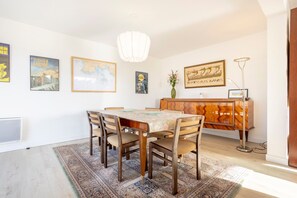 A dining area with a table, chairs, a decorative vase, a cabinet, and wall art. - Windows to the Infinite Blue – Sea View & Direct Beach Access (Concarneau)