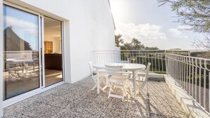 Un balcón con mesa y sillas, una puerta corrediza de vidrio y barandilla blanca.