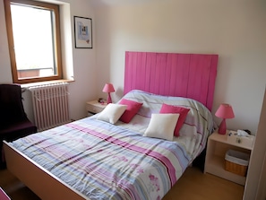 Un dormitorio con una cama, dos mesitas de noche, una silla, un radiador y una ventana.