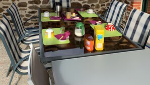 Une terrasse extérieure avec un mur en pierre, une table avec des chaises et divers aliments.