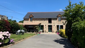 Un bâtiment en pierre de deux étages, doté d’une entrée couverte, d’une allée et entouré de verdure.