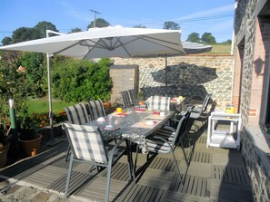 Un patio al aire libre con una mesa lista para comer, rodeada de sillas y una sombrilla grande que proporciona sombra.