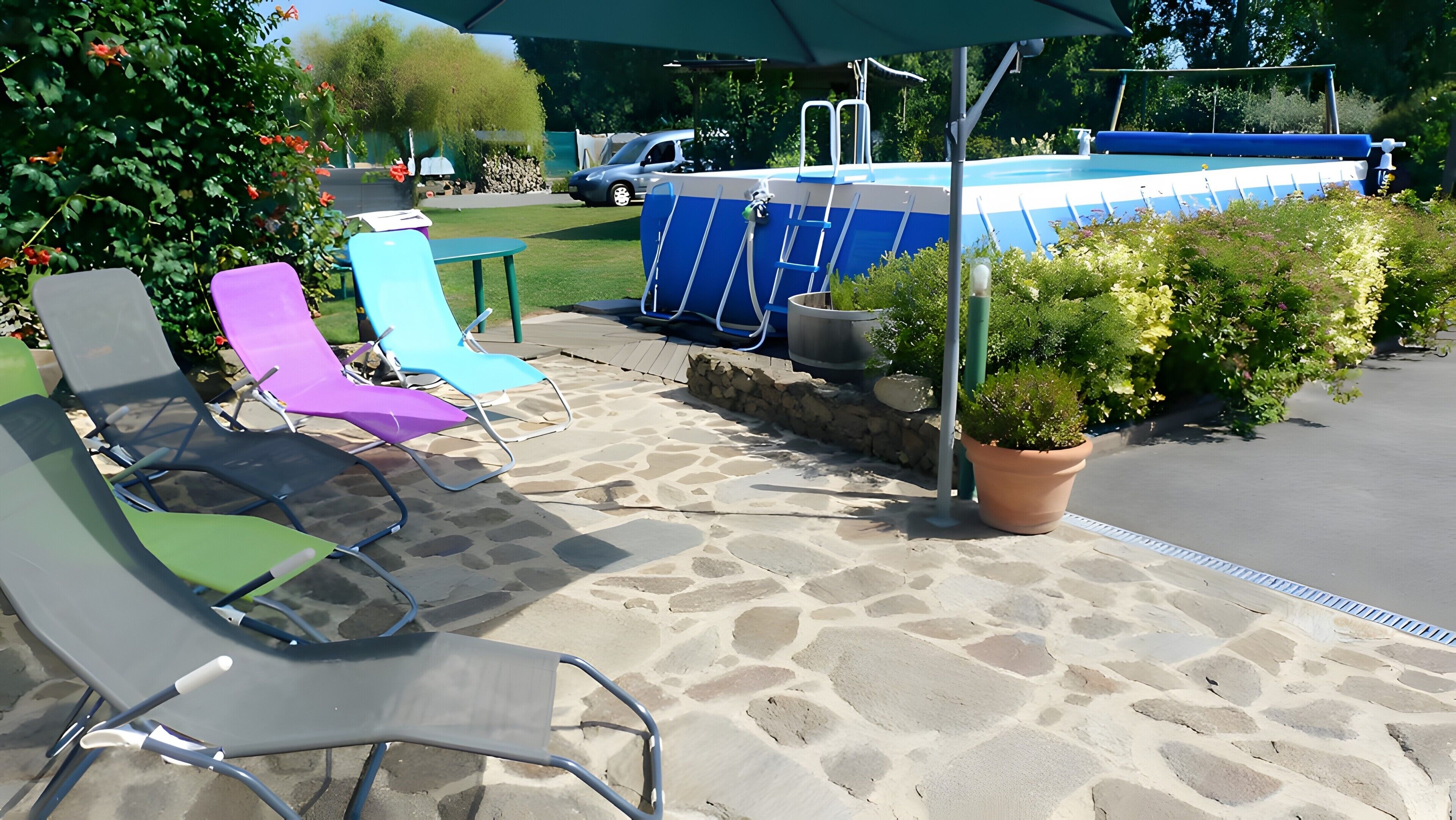 Une terrasse avec un sol en pierre, une piscine et des chaises longues.