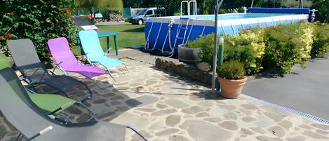 Une terrasse avec un sol en pierre, une piscine et des chaises longues.