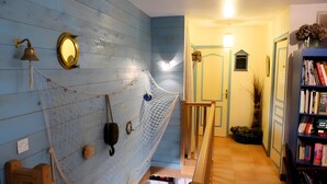 Une pièce avec un hamac, une cloche, un miroir, une bibliothèque et une porte donnant sur une autre pièce.