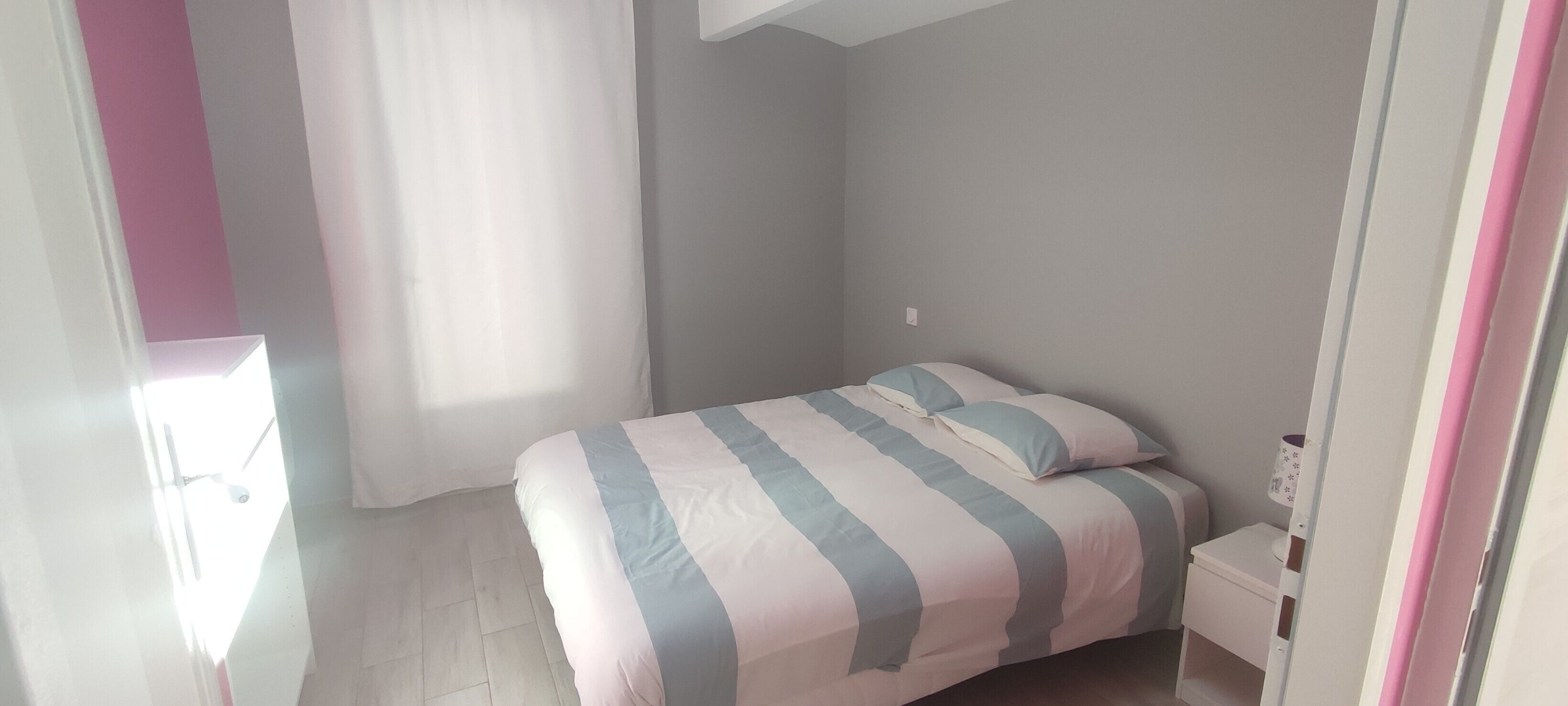 A bedroom with a bed, a nightstand, a window with curtains, and a door.