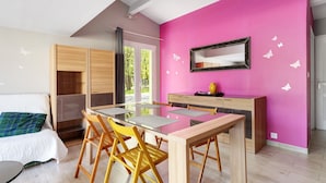 A modern room with a dining table, chairs, a bed, and a pink wall with butterfly decals.