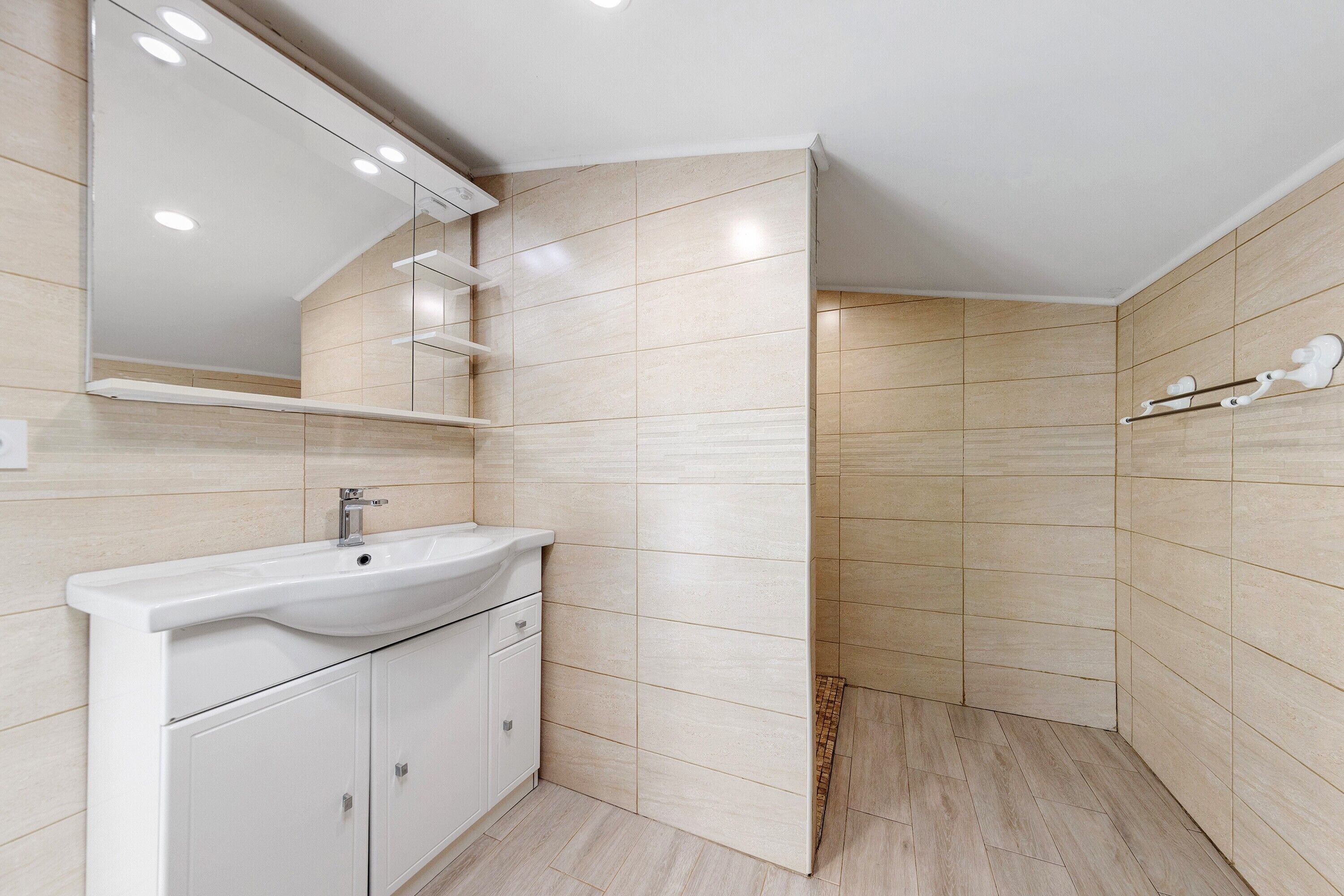A modern bathroom with a white sink, mirror, and tiled walls.