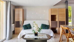 A bedroom with a bed, a nightstand, a table with chairs, and a window with curtains.