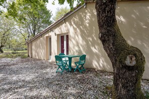 A building with a gravel ground, a tree, and a table with chairs.