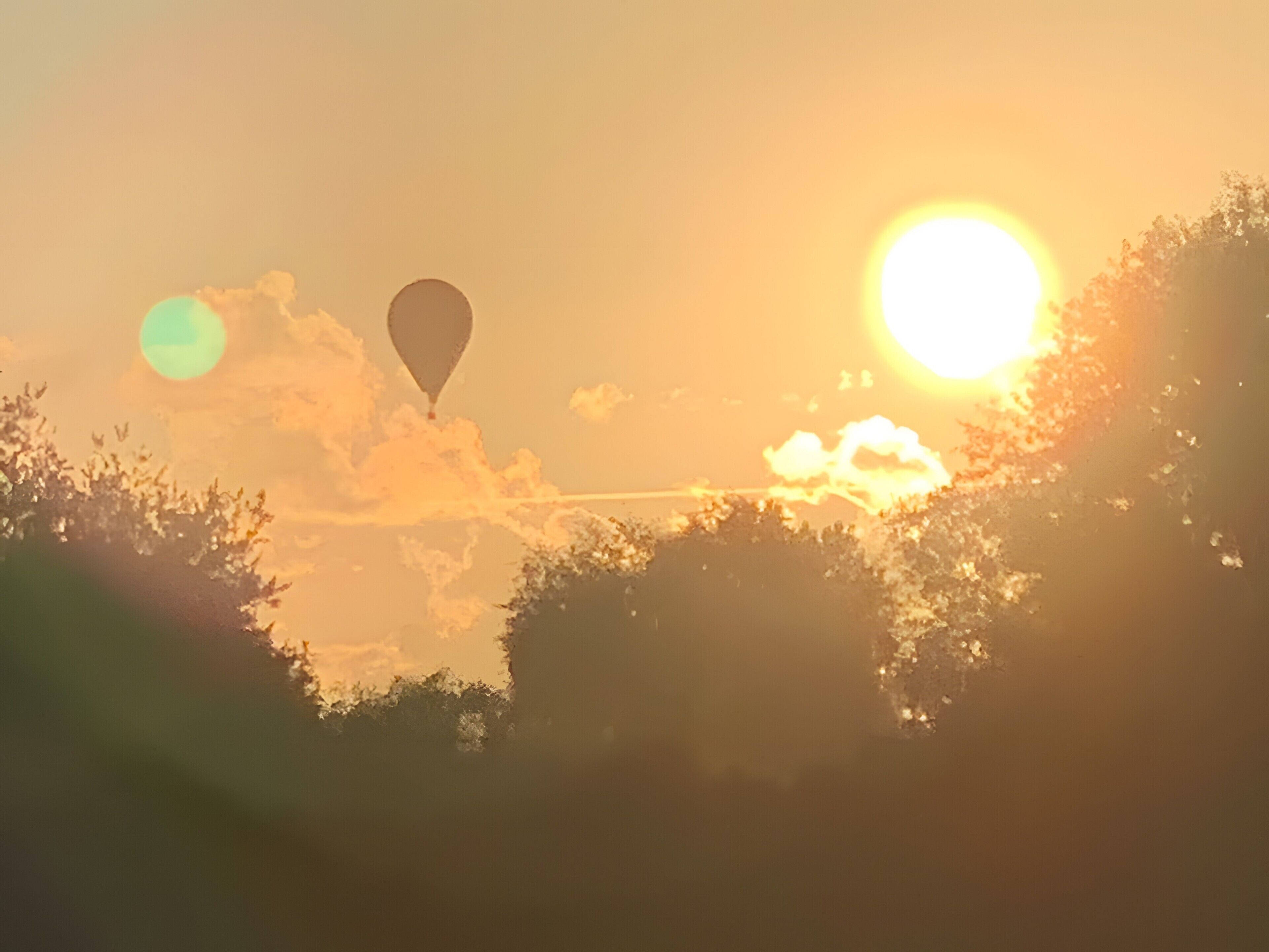 A sunset with a hot air balloon and trees in the foreground.