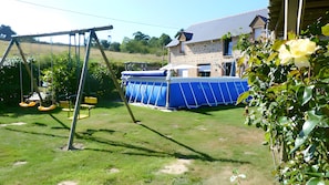 A backyard with a swing set, a pool, and a stone house. - Guest Room "Plaisir de mer" with Shared Pool, Terrace, and Wi-Fi (Saint-Guinoux)