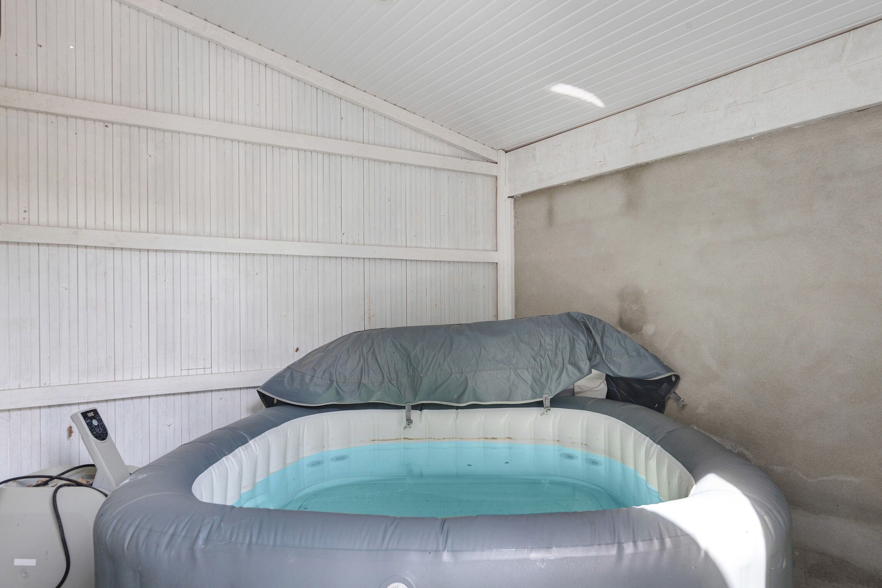 An inflatable pool with a control panel, a grey cover, and a white wall in the background.