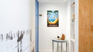 A hallway with a beach-themed poster, a small table with a vase, and a wooden door. - Bed and Breakfast 'Callune' with Wi-Fi and Air Conditioning (Capbreton)