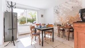 A dining area with a table, chairs, a refrigerator, and a window with a view of greenery. - Bed and Breakfast 'Callune' with Wi-Fi and Air Conditioning (Capbreton)