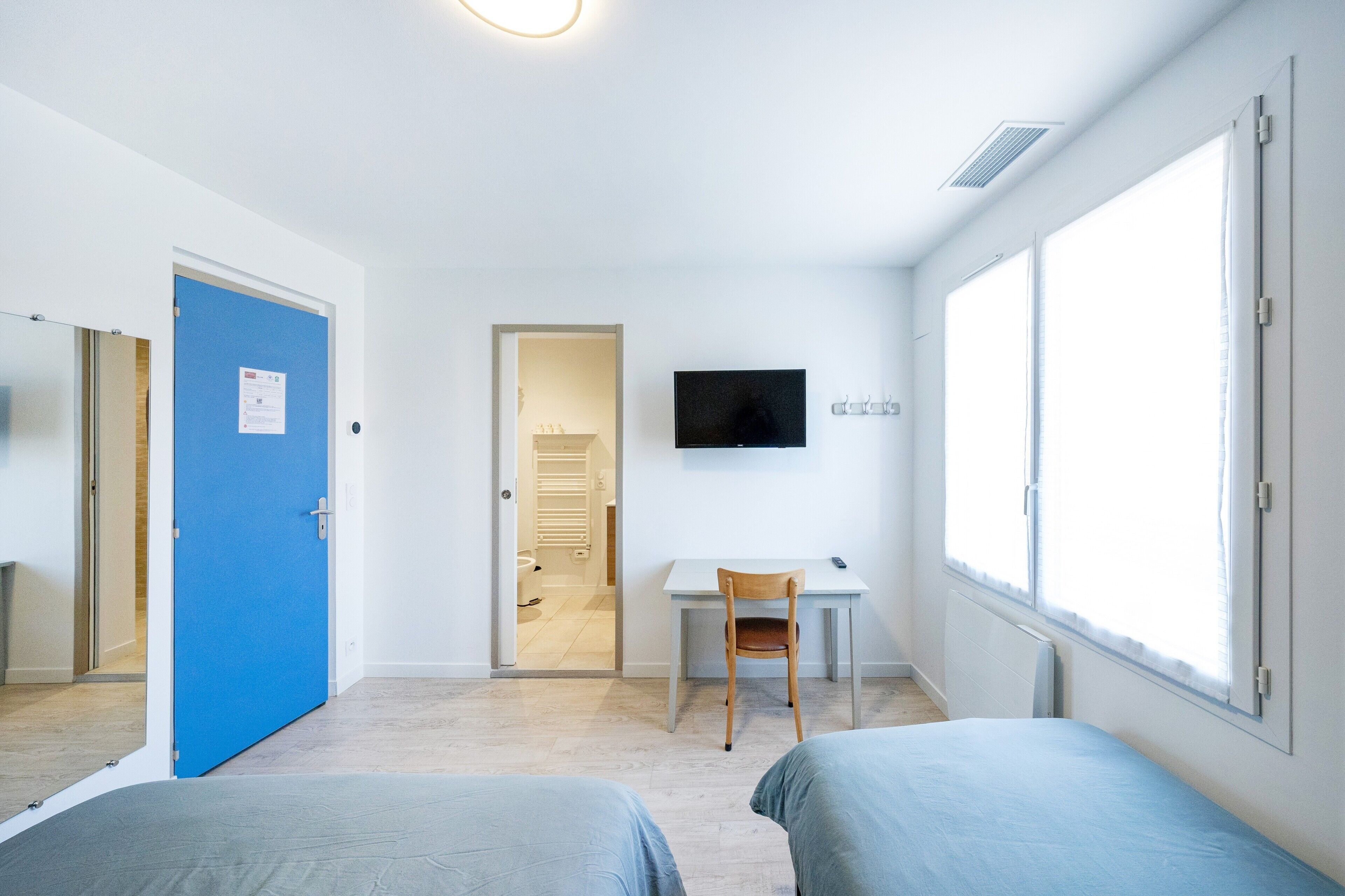 Een kamer met twee bedden, een bureau, een stoel, een televisie en een groot raam.
