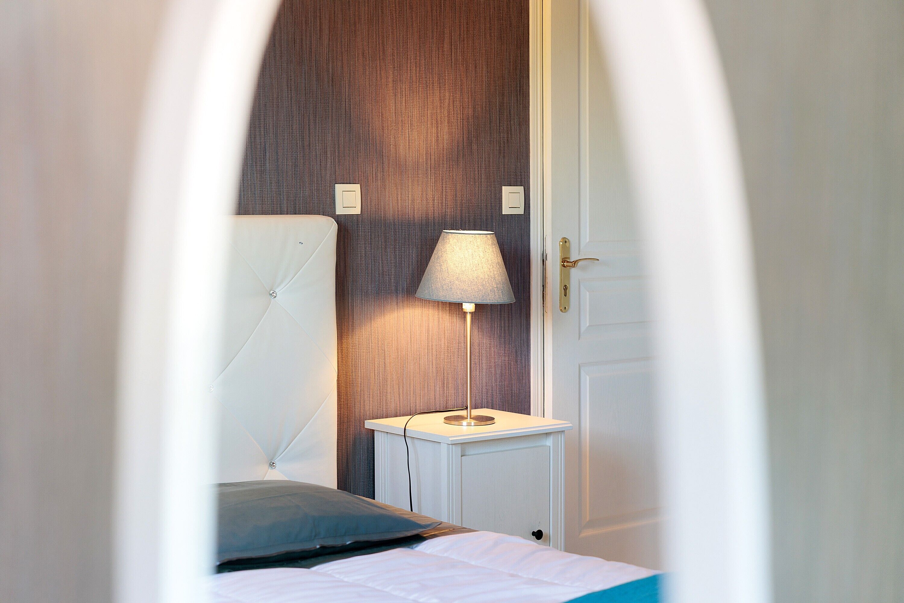 A bedroom with a bed, a bedside table with a lamp, and a door.