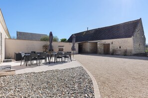 A courtyard with outdoor seating, a gravel area, and a stone building with a tiled roof. - Gîte de dino – 10 guests (Saint-Patrice)