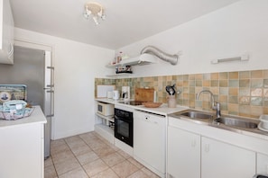 A modern kitchen with white cabinetry, a built-in oven, a dishwasher, and a stainless steel sink. - Gîte de dino – 10 guests (Saint-Patrice)