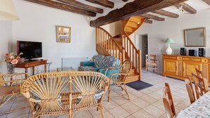 Una sala de estar con escalera de madera, muebles de mimbre, televisor y un mueble.