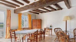 Un comedor con una mesa y sillas, vigas de madera en el techo, una ventana con cortinas y una lámpara.