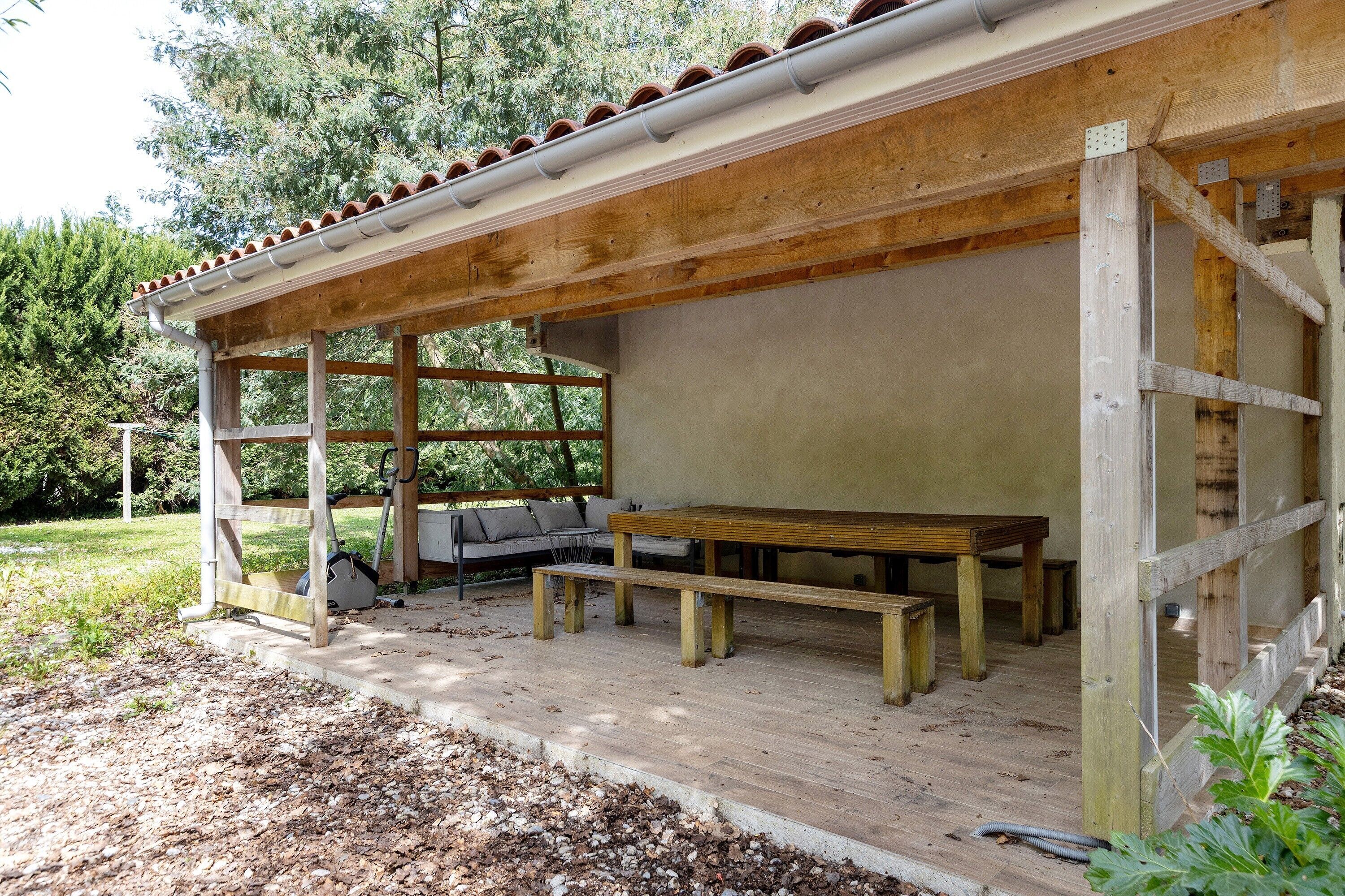 Eine Terrassenanlage aus Holz mit einer Bank und einem Tisch, umgeben von einem Holzzaun und einem überdachten Bereich mit Dach.