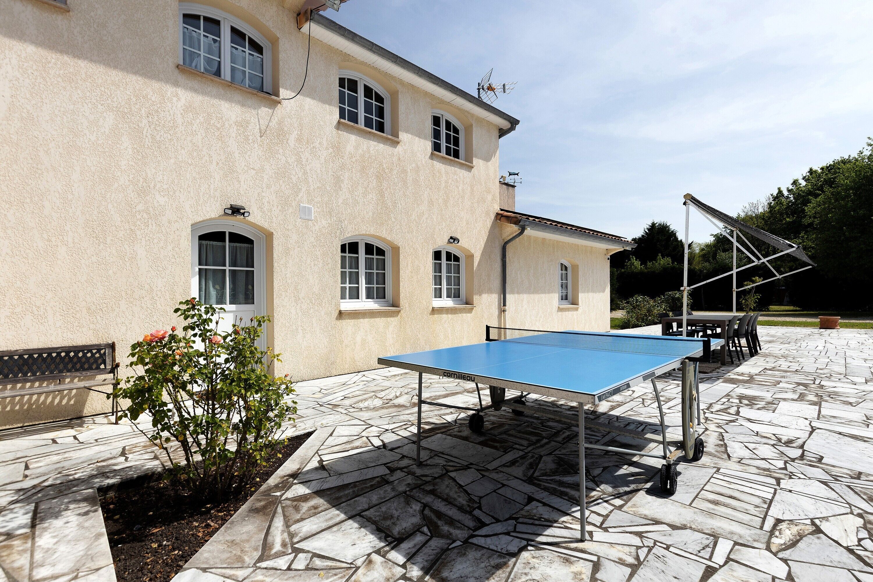 Un patio con mesa de ping pong, asientos exteriores y un edificio con amplias ventanas.