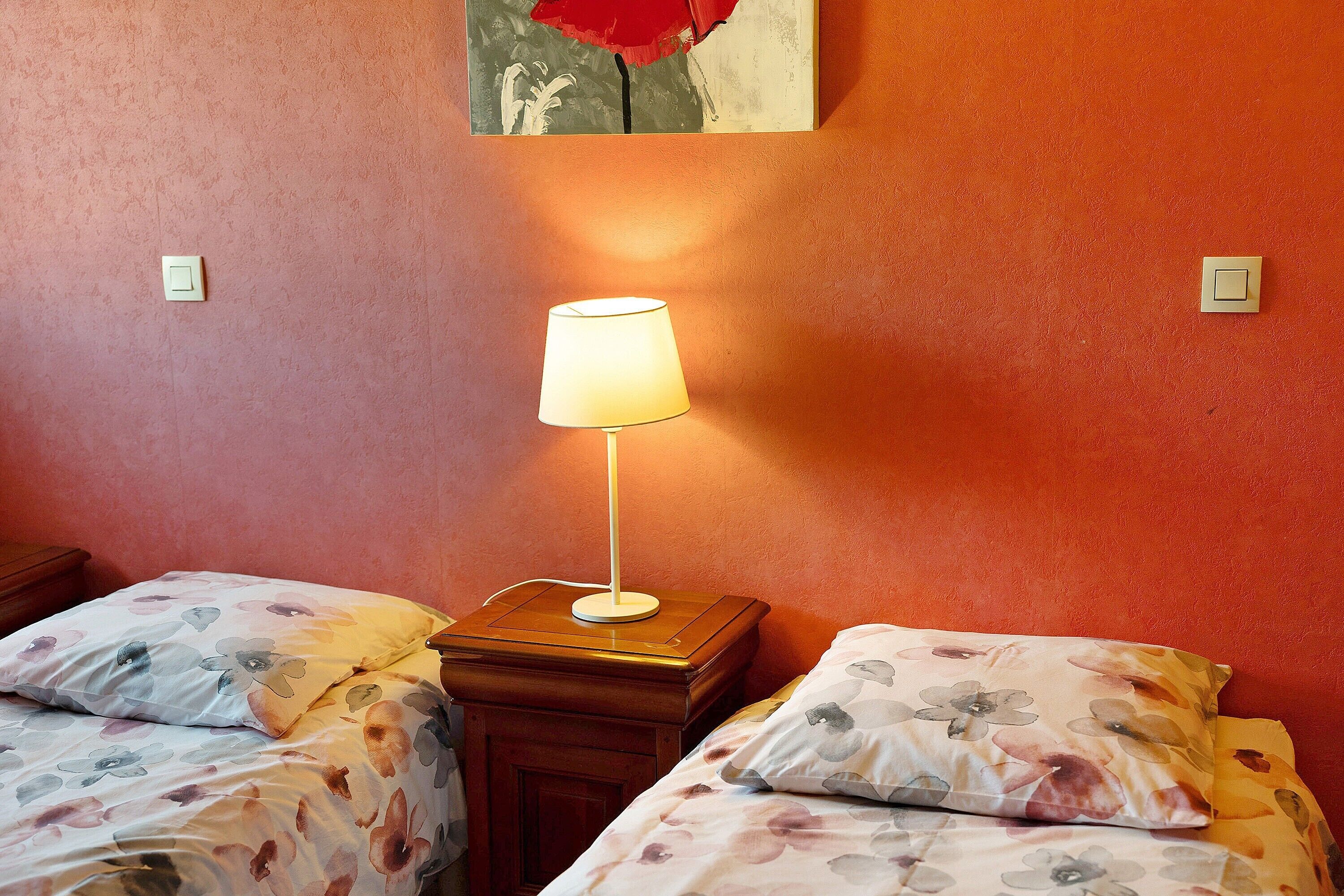 Quarto com duas camas, uma mesa de cabeceira com abajur e um quadro na parede.