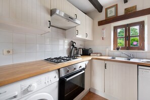 Une cuisine avec des meubles blancs, un plan de travail en bois, une cuisinière, un four, un lave-vaisselle et une fenêtre donnant sur un paysage verdoyant.