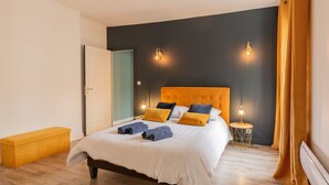 Een slaapkamer met een bed, nachtlampjes, een bankje en een deur.