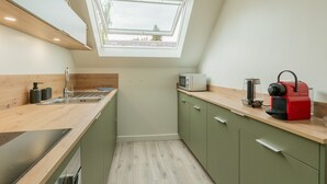Een compacte keuken met dakraam, een magnetron, waterkoker en een rode koffiezetapparaat op het aanrecht.