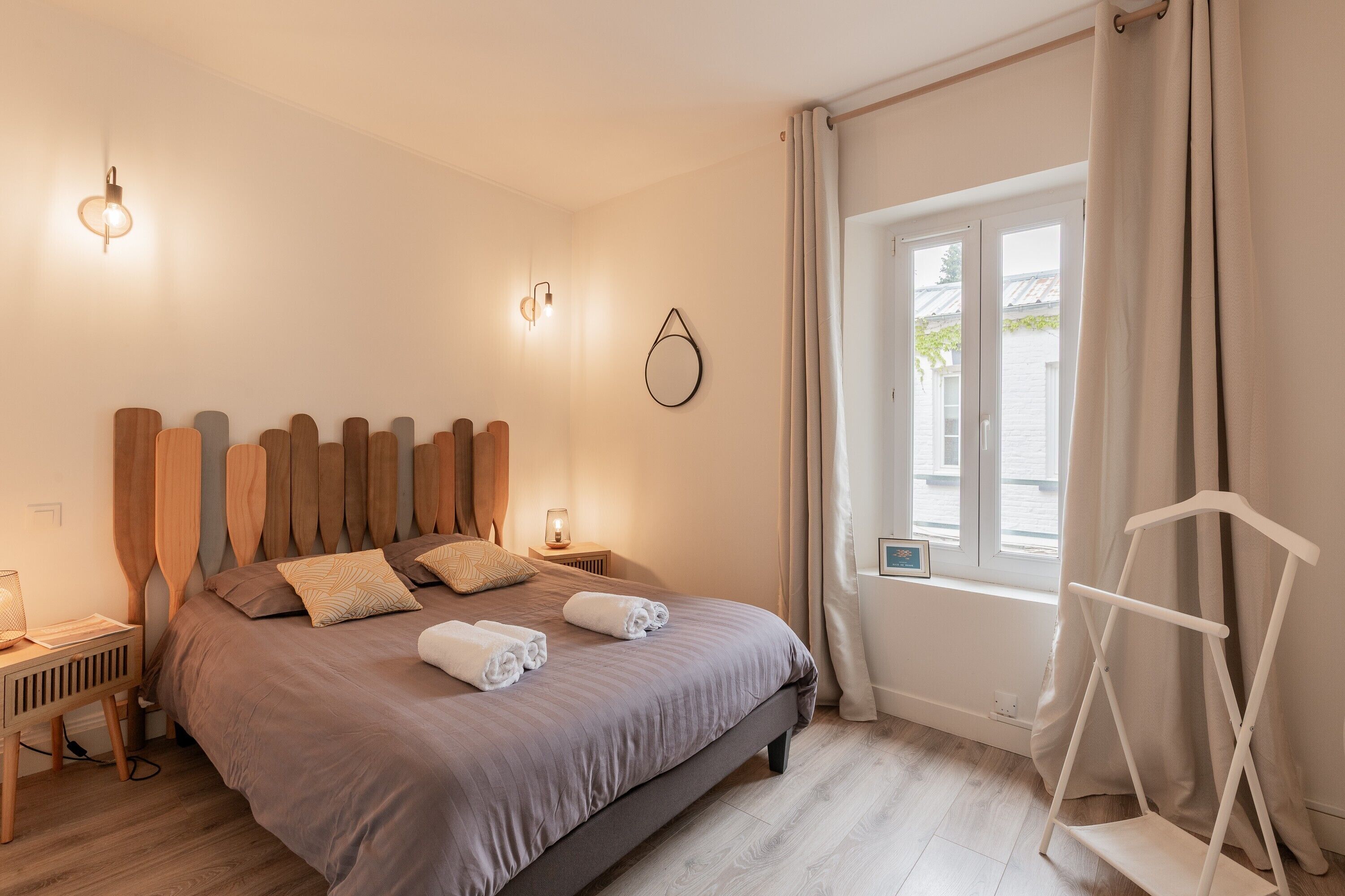 A bedroom with a bed, bedside lamps, a window with curtains, and a white chair.