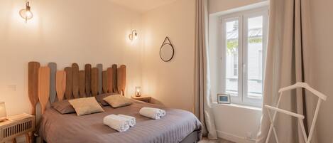 A bedroom with a bed, bedside lamps, a window with curtains, and a white chair.