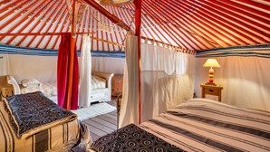 Une yourte traditionnelle, avec un lit, une chaise et une petite table sur laquelle se trouve une lampe.