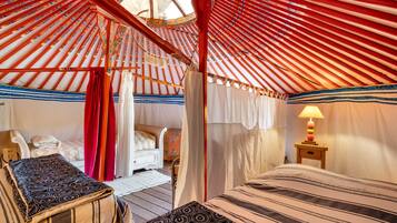 Une yourte traditionnelle, avec un lit, une chaise et une petite table sur laquelle se trouve une lampe.