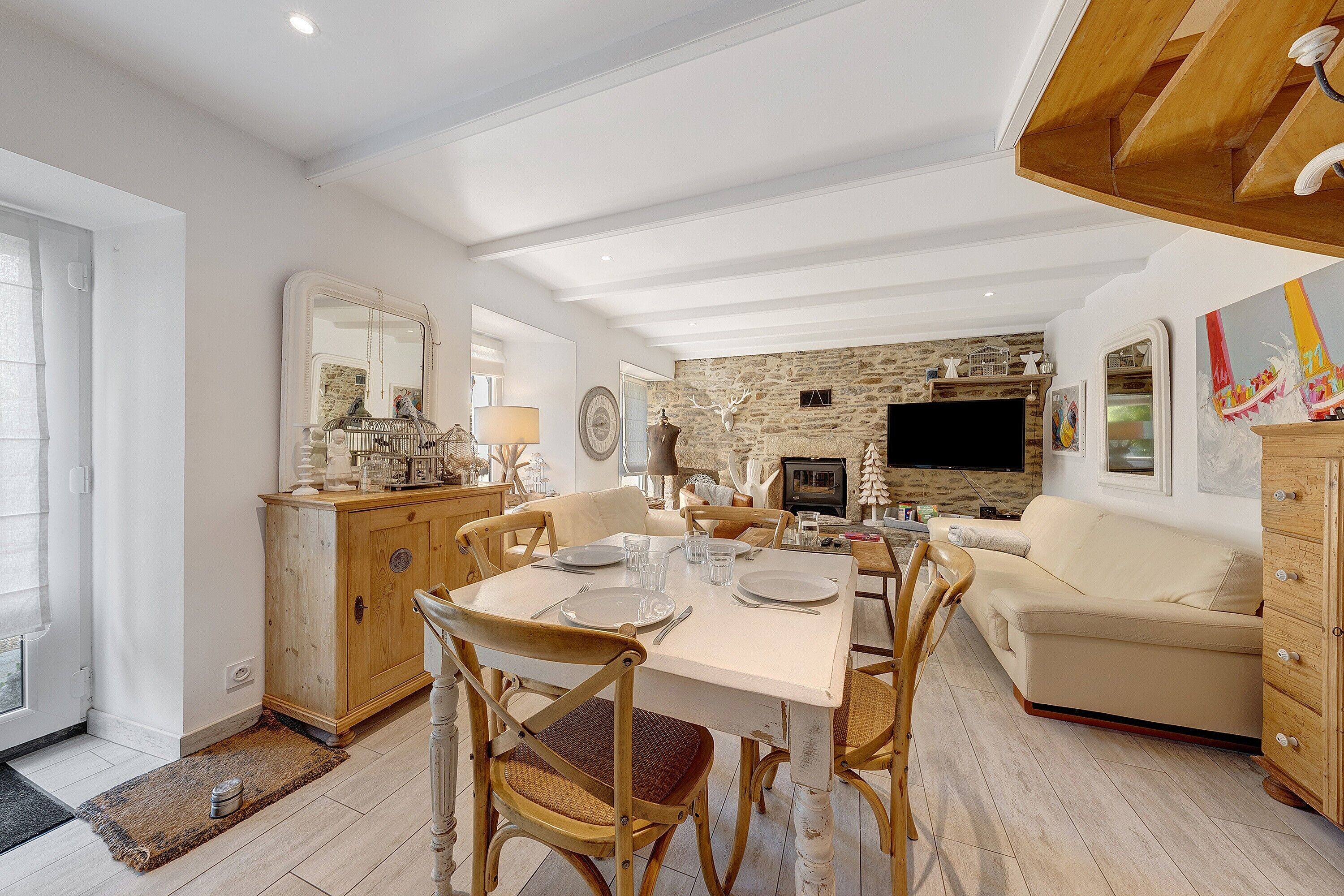 A dining area with a table set for four, wooden chairs, a stone fireplace, and a television.