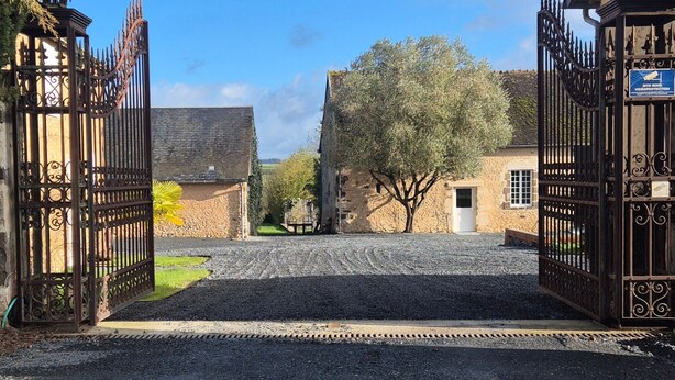 A gravel driveway leading to a gated entrance with a stone building in the background.