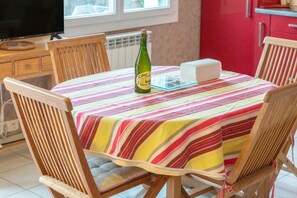 Une table à manger recouverte d’une nappe à rayures, des chaises en bois, une bouteille de champagne Clore et un gâteau présenté sur un présentoir en verre.
