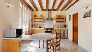 A kitchen with a round table, wooden chairs, a microwave, cabinets, and a stove. - Gite la clématite – In the Heart of the Loire Castles (Mosnes)