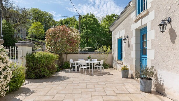 A patio with a table and chairs, a potted plant, and a building with blue shutters. - Gite la clématite – In the Heart of the Loire Castles (Mosnes)
