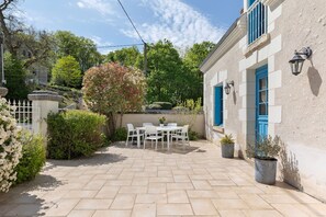 A patio with a table and chairs, a potted plant, and a building with blue shutters. - Gite la clématite – In the Heart of the Loire Castles (Mosnes)