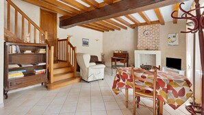 A living room with a fireplace, wooden beams, a sofa, a table, and a bookshelf. - Gite la clématite – In the Heart of the Loire Castles (Mosnes)